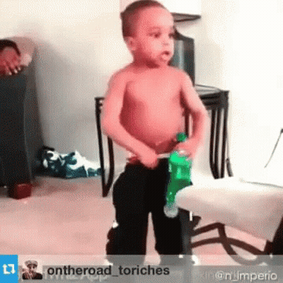 A Little Boy Without A Shirt Is Holding A Green Bottle Of Soda . GIF