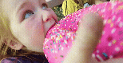 A Little Girl Eating A Pink Donut With Sprinkles GIF