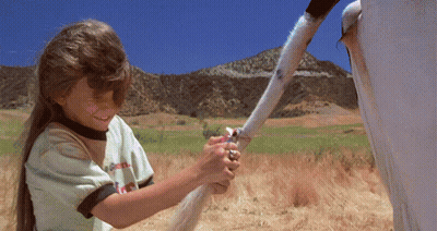 A Little Girl Holding A Horse 'S Tail In A Field Wearing A Shirt That Says ' Coca Cola ' On It GIF
