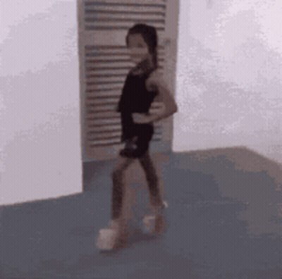 A Little Girl In A Black Dress Is Standing In A Room . GIF