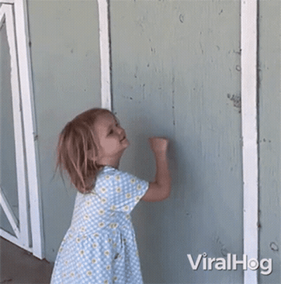 A Little Girl In A Blue And Yellow Dress Is Standing In Front Of A Wall . GIF