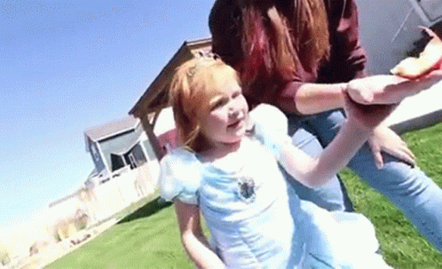 A Little Girl In A Blue Dress Is Being Held By A Woman In A Princess Costume . GIF