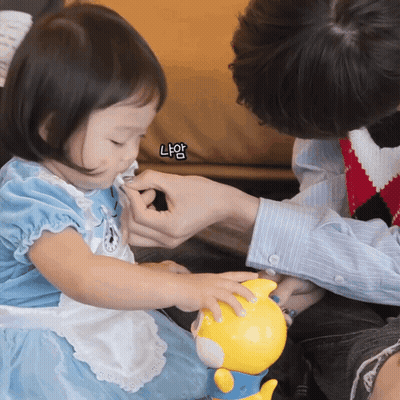 A Little Girl In A Blue Dress Is Playing With A Yellow Toy While A Man Holds Her Hand GIF