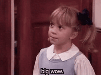 A Little Girl In A Blue Dress Is Standing In Front Of A Door . GIF