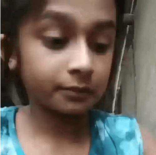 A Little Girl In A Blue Dress Looks At The Camera GIF