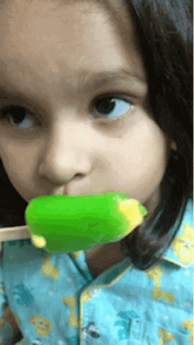 A Little Girl In A Blue Shirt Is Eating A Green Ice Cream Bar GIF