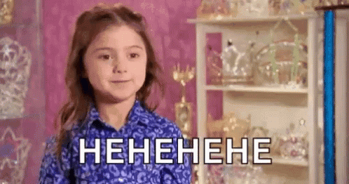 A Little Girl In A Blue Shirt Is Laughing In Front Of A Shelf With Tiaras On It . GIF