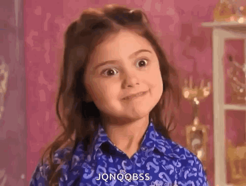 A Little Girl In A Blue Shirt Is Making A Funny Face And Smiling . GIF