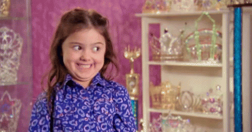 A Little Girl In A Blue Shirt Is Making A Funny Face In Front Of A Shelf Full Of Crowns . GIF