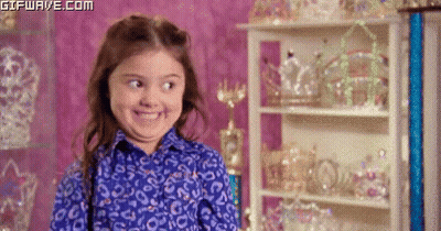 A Little Girl In A Blue Shirt Is Smiling In Front Of A Display Of Tiaras . GIF