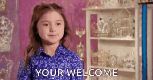 A Little Girl In A Blue Shirt Is Standing In Front Of A Shelf . GIF