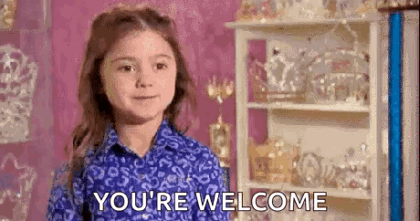 A Little Girl In A Blue Shirt Is Standing In Front Of A Shelf With A Crown On It . GIF