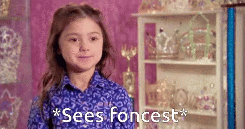 A Little Girl In A Blue Shirt Is Standing In Front Of A Shelf With The Words " Sees Foncrest " Written On It . GIF