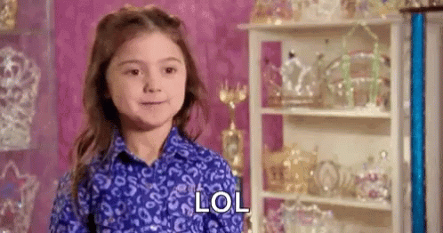 A Little Girl In A Blue Shirt Is Standing In Front Of A Shelf With Tiaras On It And Says Lol . GIF
