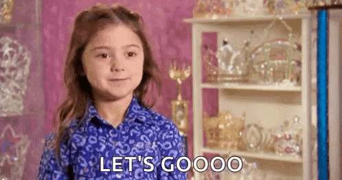 A Little Girl In A Blue Shirt Is Standing In Front Of A Shelf With Tiaras On It . GIF