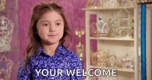 A Little Girl In A Blue Shirt Is Standing In Front Of A Shelf With Trophies And Says `` Your Welcome '' . GIF