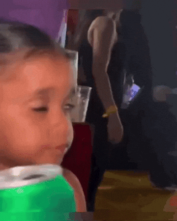 A Little Girl In A Green Shirt Is Looking At The Camera . GIF