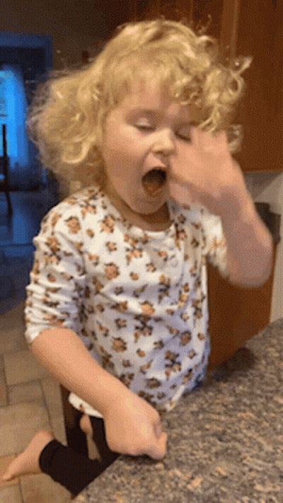A Little Girl In A Leopard Print Shirt Is Sitting On A Counter With Her Mouth Open GIF