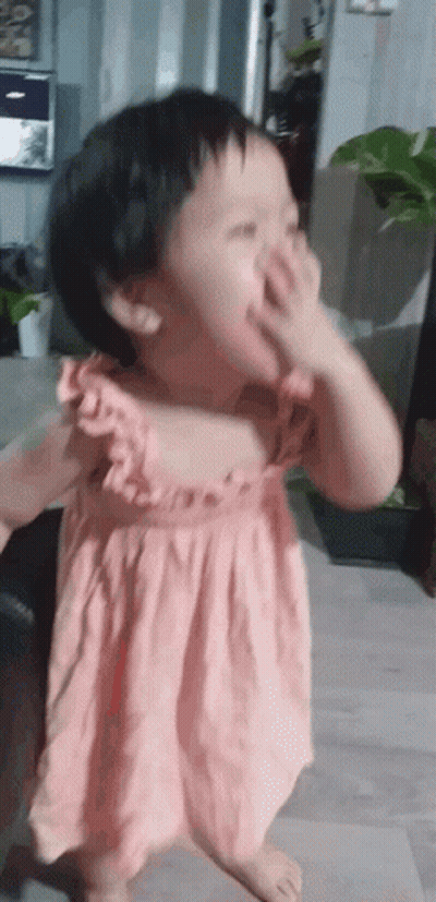 A Little Girl In A Pink Dress Covering Her Face With Her Hand GIF