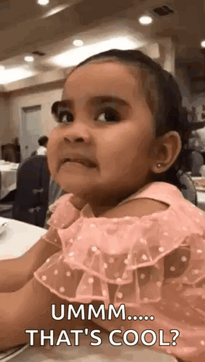A Little Girl In A Pink Dress Is Sitting At A Table And Making A Face . GIF