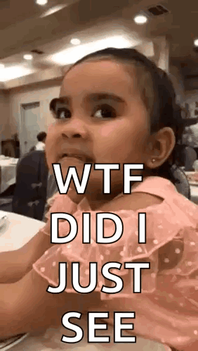 A Little Girl In A Pink Dress Is Sitting At A Table And Making A Face . GIF