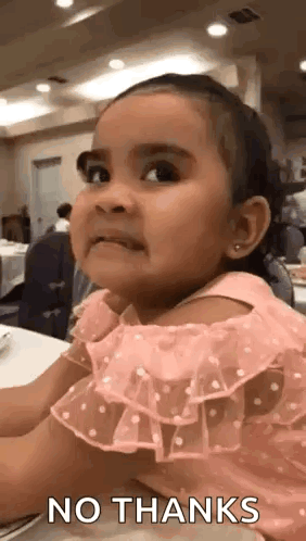 A Little Girl In A Pink Dress Is Sitting At A Table With A No Thanks Sign On Her Face . GIF
