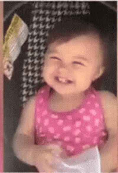 A Little Girl In A Pink Dress Is Smiling While Sitting In A Stroller GIF