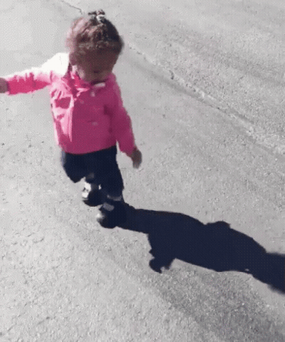 A Little Girl In A Pink Jacket Is Running Down A Road . GIF