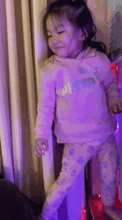 A Little Girl In A Pink Shirt And Pants Is Standing On A Red Carpet . GIF