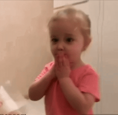A Little Girl In A Pink Shirt Is Covering Her Mouth With Her Hands In A Bathroom . GIF