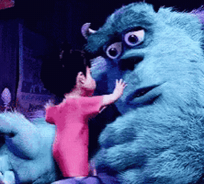 A Little Girl In A Pink Shirt Is Standing Next To A Blue Monster GIF