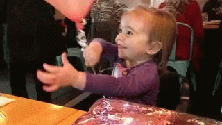 A Little Girl In A Purple Shirt Is Holding A Balloon In Her Hand GIF