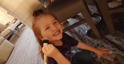 A Little Girl In A Purple Shirt Is Smiling While Holding A Brush In Her Hand GIF