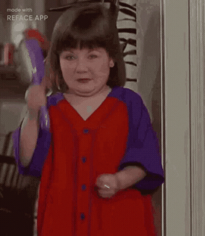 A Little Girl In A Red And Purple Dress Is Standing In A Doorway . GIF