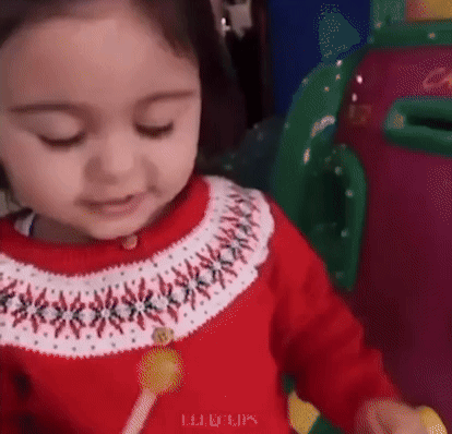 A Little Girl In A Red And White Sweater Is Holding A Lollipop . GIF