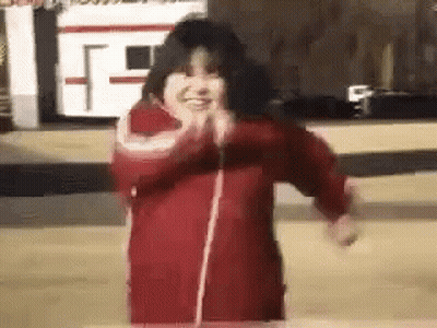 A Little Girl In A Red Jacket Is Dancing In Front Of A Camera . GIF