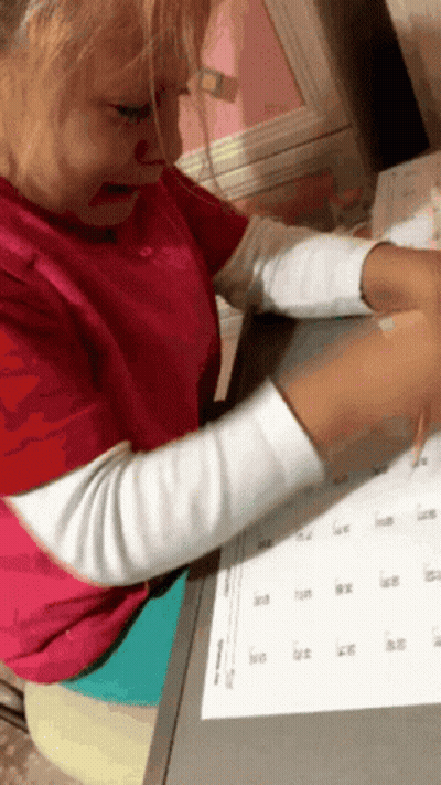 A Little Girl In A Red Shirt Is Sitting At A Desk With A Calendar On It GIF