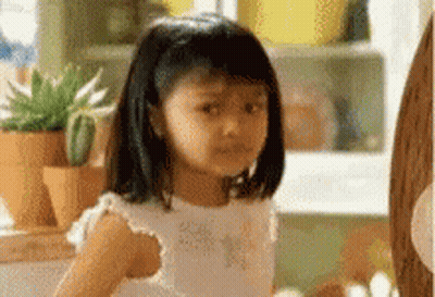 A Little Girl In A White Dress Is Sitting In Front Of A Window . GIF