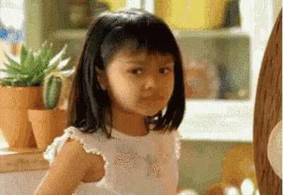A Little Girl In A White Dress Is Standing In Front Of Potted Plants In A Kitchen . GIF