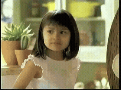 A Little Girl In A White Dress Is Standing In Front Of Potted Plants GIF