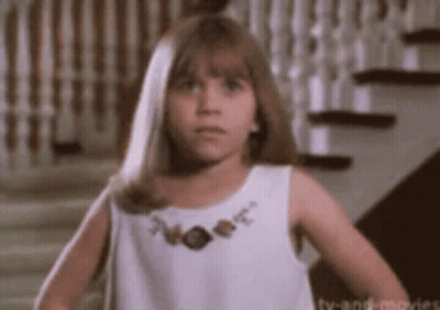 A Little Girl In A White Dress Is Standing In Front Of Stairs . GIF