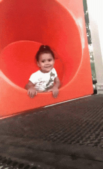 A Little Girl In A White Shirt Is Sitting On A Red Slide GIF