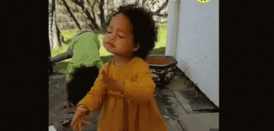 A Little Girl In A Yellow Dress Is Dancing In Front Of A Potted Plant And A Man In A Green Shirt . GIF