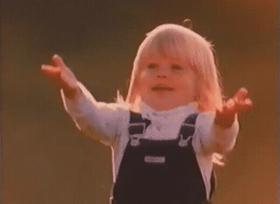 A Little Girl In Overalls Is Standing With Her Arms Outstretched In A Field . GIF