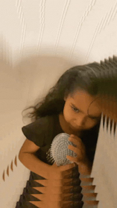 A Little Girl Is Brushing Her Hair In Front Of A Mirror GIF