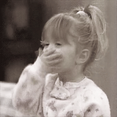 A Little Girl Is Covering Her Mouth With Her Hand And Smiling . GIF