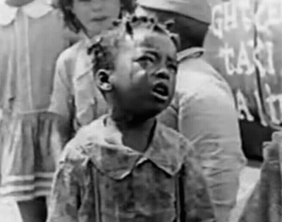 A Little Girl Is Crying In A Black And White Photo While Standing In Front Of A Sign . GIF