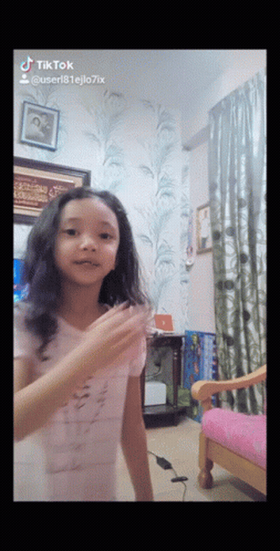 A Little Girl Is Dancing In A Room With A Pink Chair And A Picture On The Wall That Says Tiktok GIF