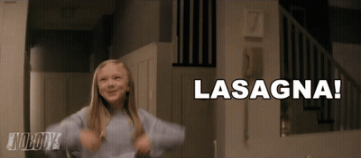 A Little Girl Is Dancing In Front Of A Sign That Says Lasagna On It GIF