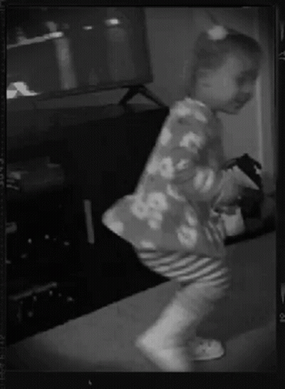 A Little Girl Is Dancing In Front Of A Tv In A Black And White Photo GIF